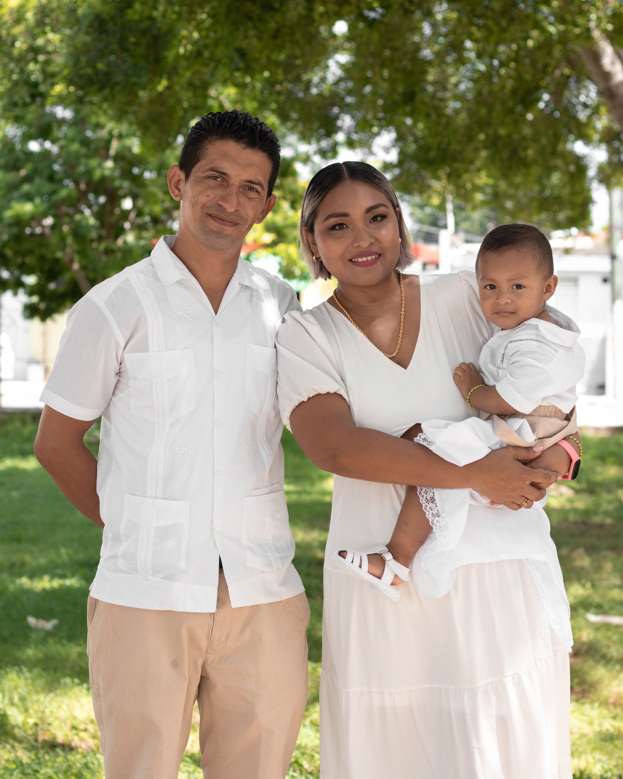 Portrait of a smiling family posed together in a sunny outdoor setting.